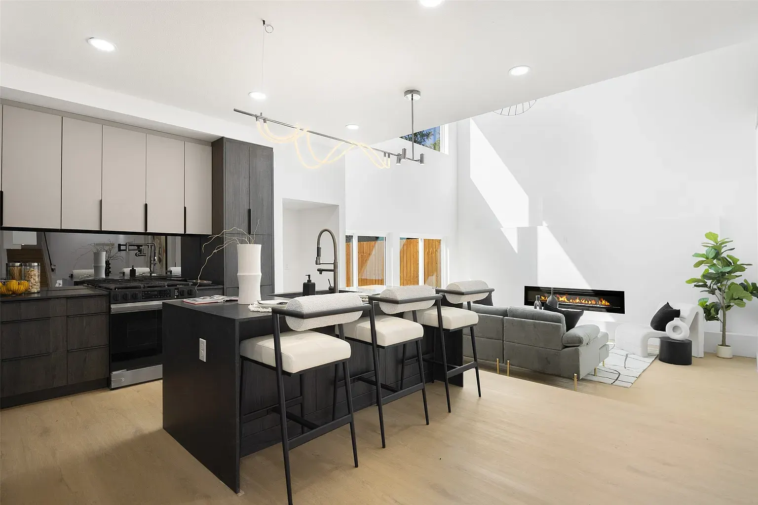 A modern kitchen with dark cabinets opening to a bright living area