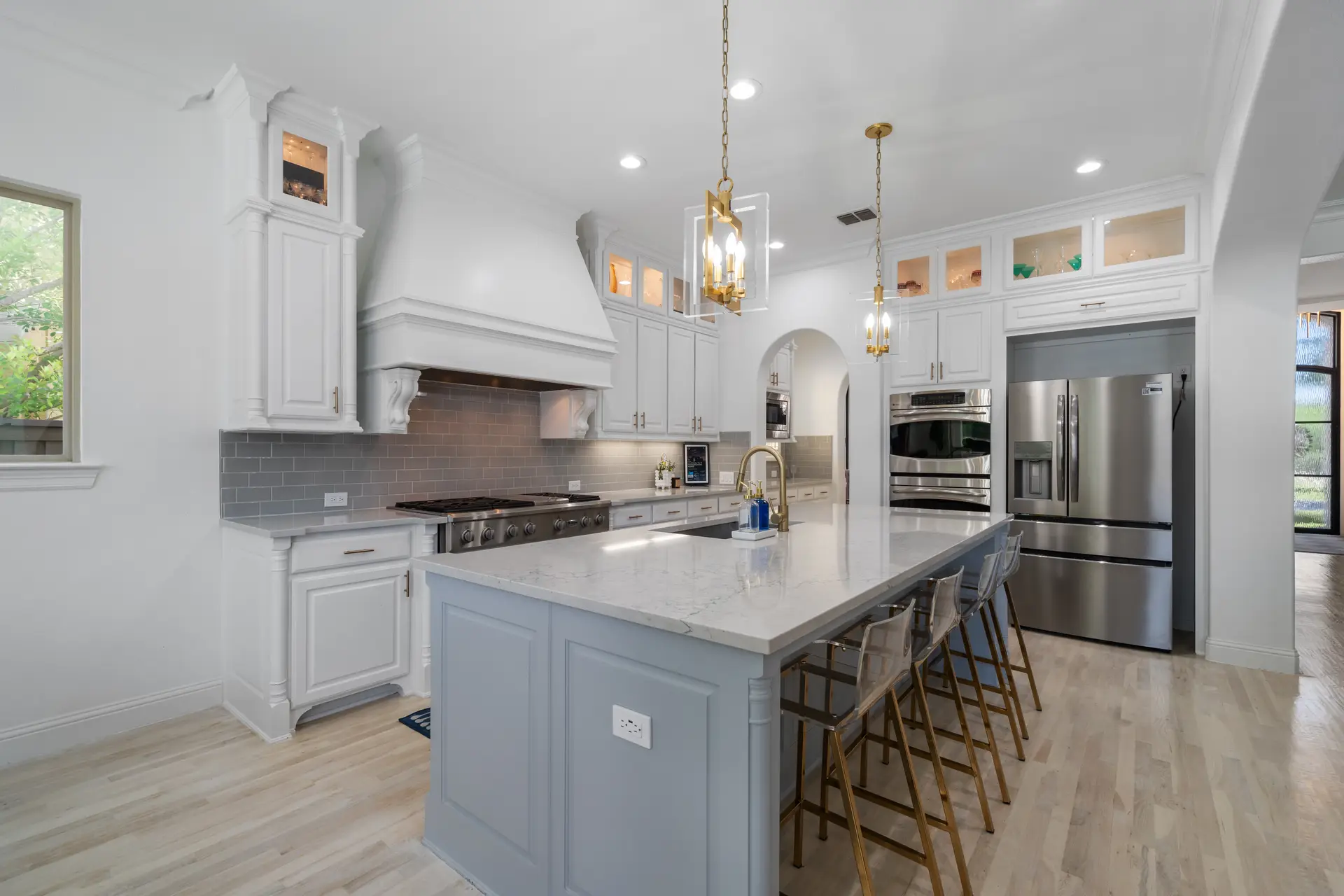 A bright white kitchen with a gray island and pendant lights