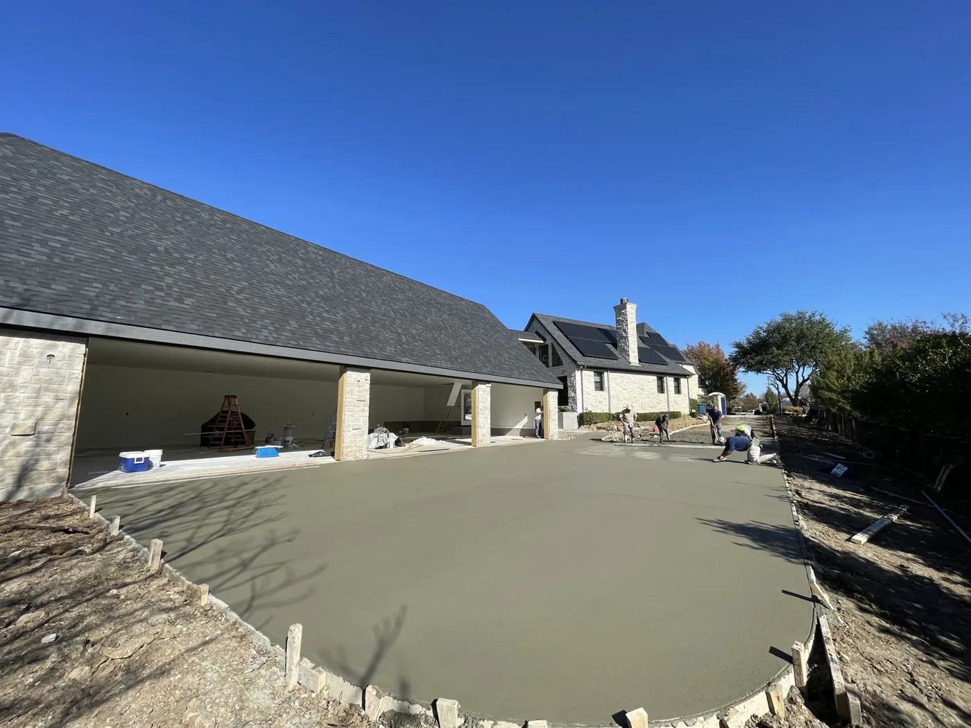 Crew finishing a large concrete driveway pour at a new stone garage
