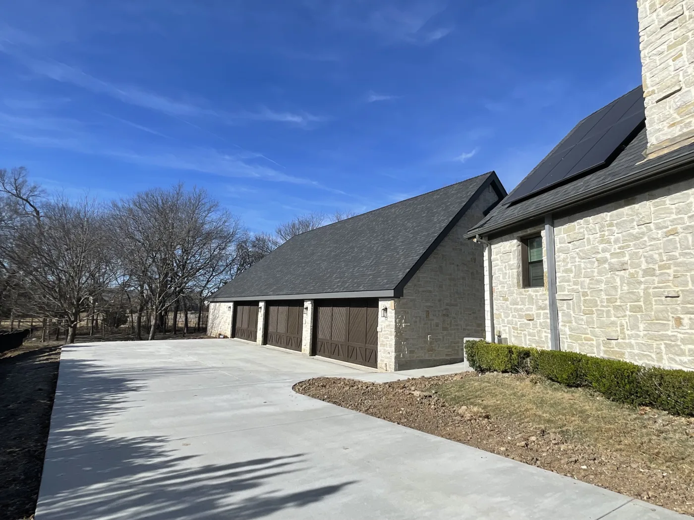 New architectural shingle roof on a stone garage with a fresh concrete driveway