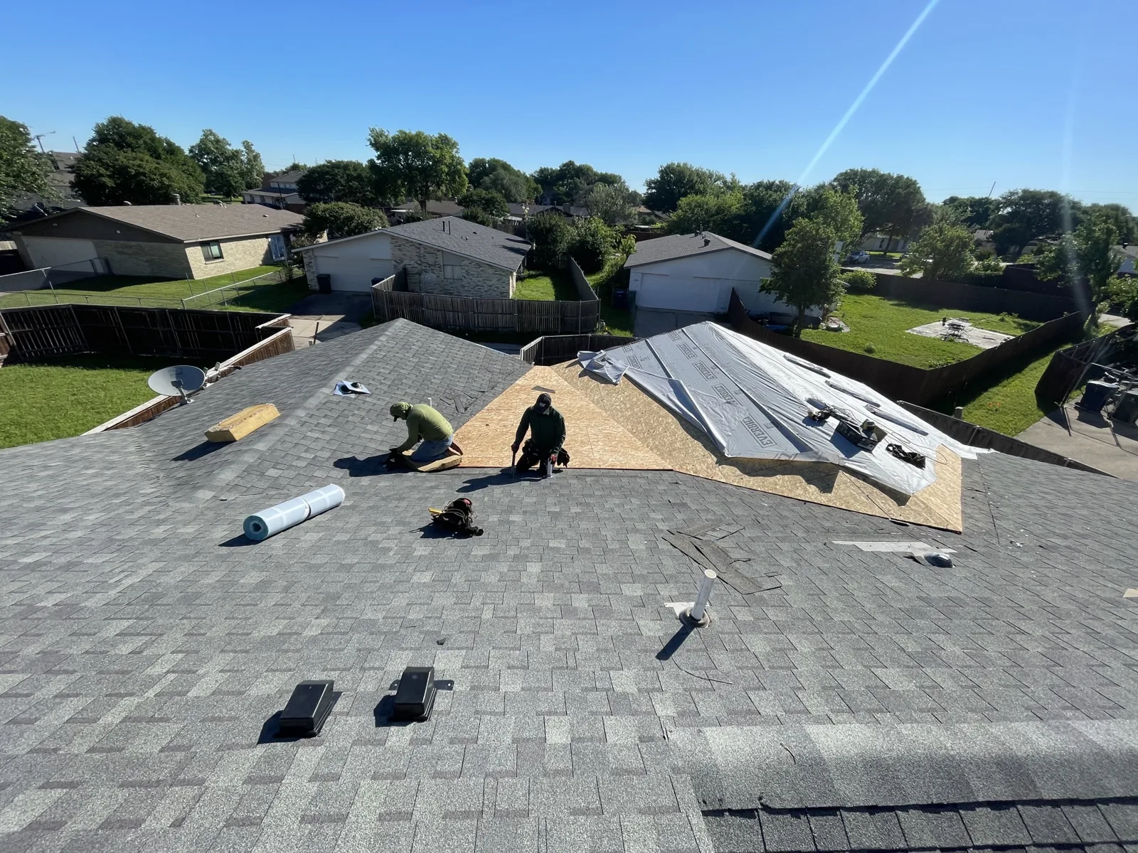 Roofing crew installing shingles above a newly built patio